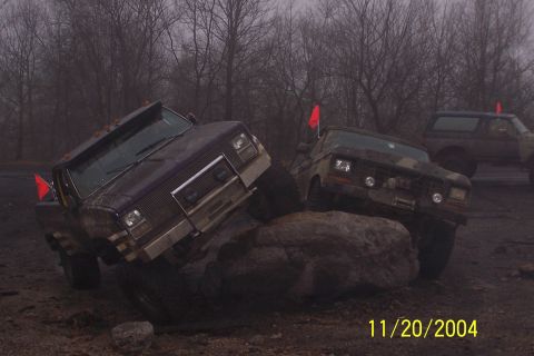 1979 Ford Bronco - Two off-road trucks navigate a rocky, muddy terrain under an overcast sky.