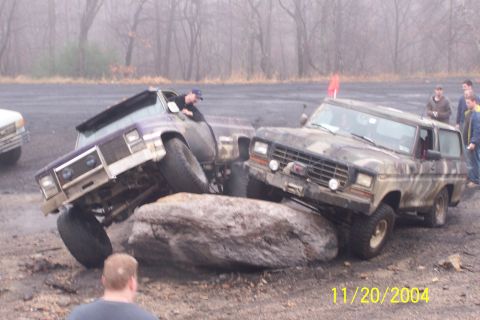 1979 Ford Bronco - Two off-road vehicles are shown attempting to maneuver over a large rock obstacle.
