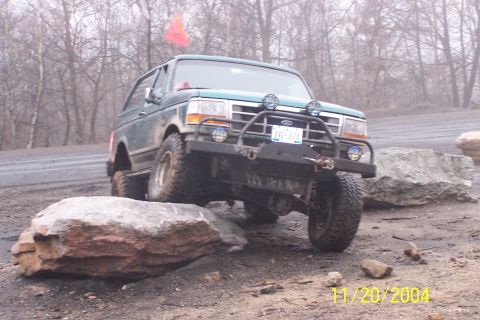 1979 Ford Bronco - A green Ford Bronco navigates a rocky terrain with a red flag on its roof.