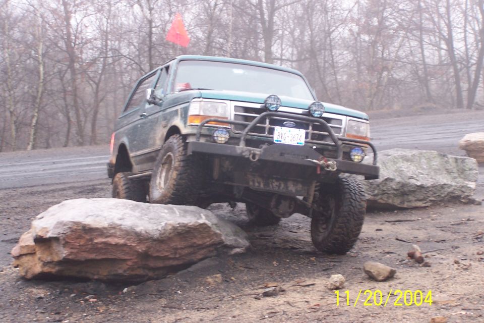 Green Ford Bronco with off-road tires climbing over rocks