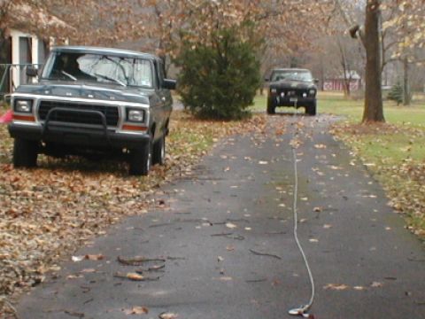 1979 Ford Bronco - A dark green 1979 Ford Bronco is parked on a leaf-covered driveway, with another vehicle visible in the distance.