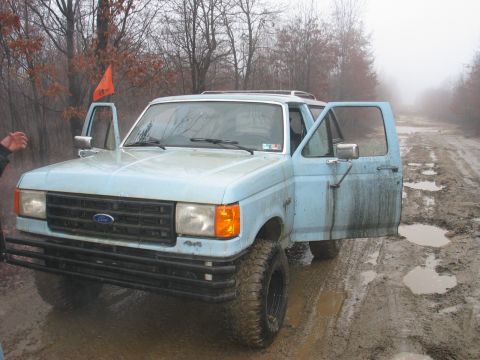 1995 Ford Bronco - Muddy road conditions with a light blue pickup truck, driver's side doors open.
