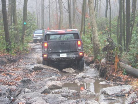 1995 Ford Bronco - Two SUVs navigate a challenging off-road course with water and rocks.