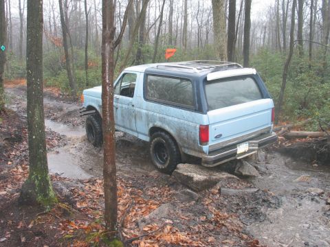 1995 Ford Bronco - Ford Bronco tackles a challenging muddy obstacle on an off-road trail.