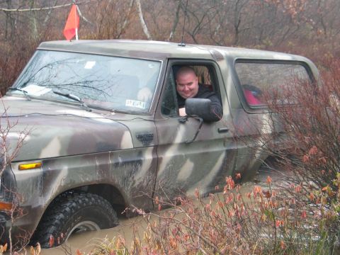 1995 Ford Bronco - Camouflaged Ford Bronco is stuck in mud with a man inside.