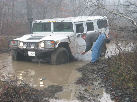 1995 Ford Bronco - A person inspects the water level around a stuck Hummer H1 in a muddy off-road area.