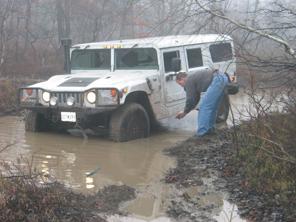 White Hummer H1 stuck in a muddy puddle with a person checking the water