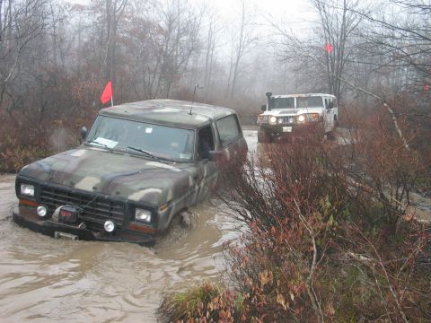 1995 Ford Bronco - A camouflaged Ford Bronco navigates a muddy off-road course, followed by a white Humvee.