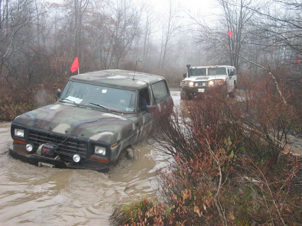 Camouflaged 1978 Ford Bronco stuck in mud, front winch visible