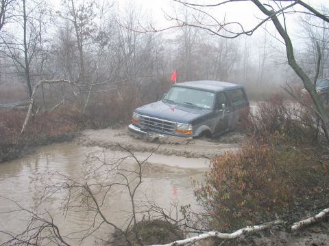1995 Ford Bronco - A 1995 Ford Bronco navigates a challenging muddy off-road course on a foggy day.