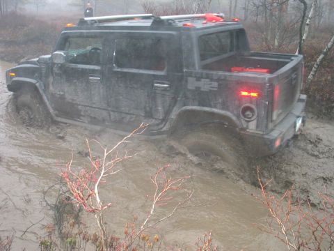 1995 Ford Bronco - Hummer H2 navigates through a muddy off-road trail, tires deep in the mire.