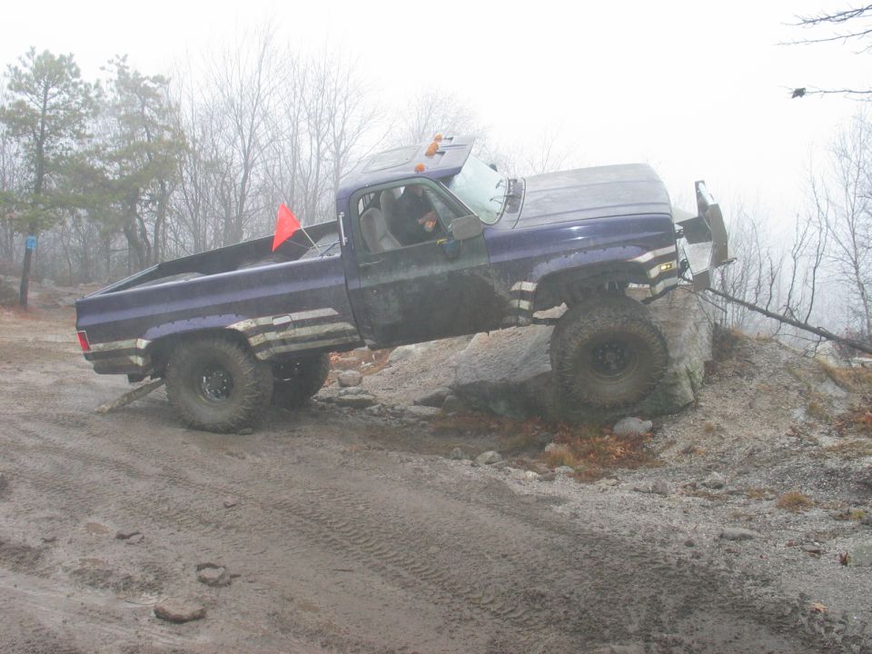 Purple pickup truck with off-road tires climbing over rocks on a muddy trail