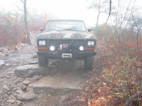 1995 Ford Bronco - A camouflaged Ford Bronco navigates a challenging, rocky, and muddy off-road path.