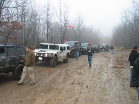 1995 Ford Bronco - Multiple off-road vehicles drive down a muddy path on a foggy day.