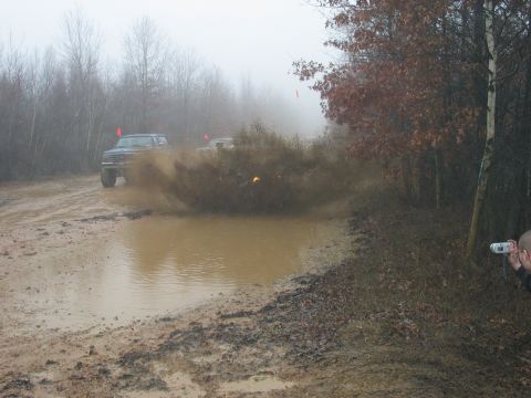1995 Ford Bronco - Two off-road vehicles navigate a muddy trail, creating a significant splash as one drives through a deep puddle.