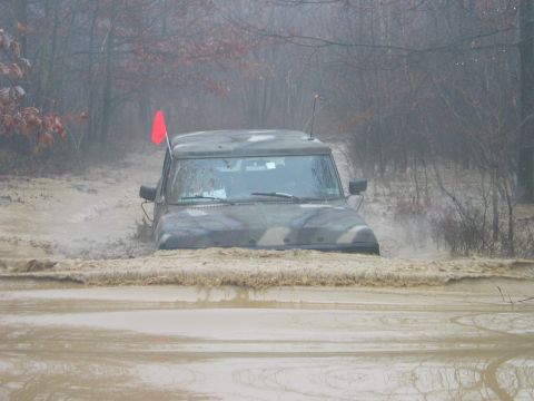 1995 Ford Bronco - Off-road vehicle navigates a flooded, muddy terrain with trees in the background.