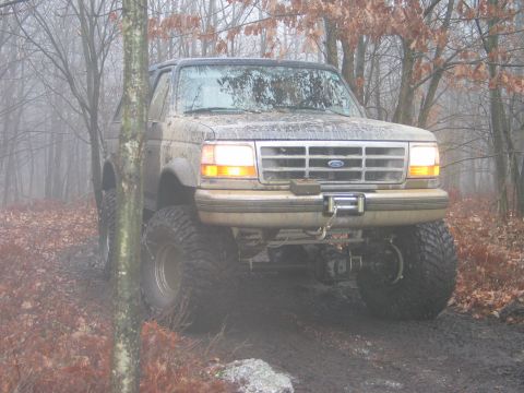 1995 Ford Bronco - Muddy 1995 Ford Bronco navigates a wooded trail with large off-road tires.