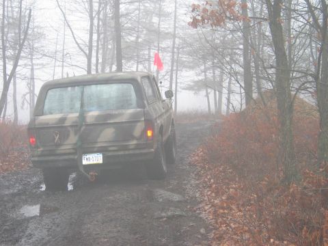 1995 Ford Bronco - A camouflaged Ford Bronco navigates a muddy path through a foggy forest.