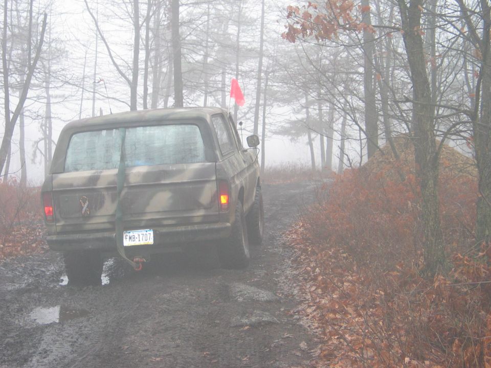 Camouflaged Ford Bronco on a muddy forest road, rear view. License plate FMB-1707
