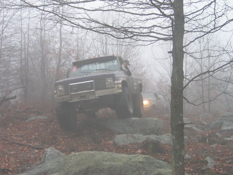 Dark pickup truck with off-road tires navigating rocky terrain in fog