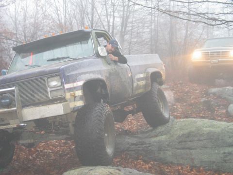 1995 Ford Bronco - Two modified pickup trucks navigate a rocky off-road trail in foggy conditions.