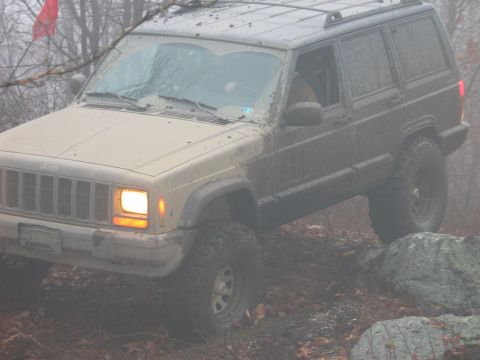 1995 Ford Bronco - A muddy Jeep Cherokee XJ navigates rocky terrain in foggy conditions.