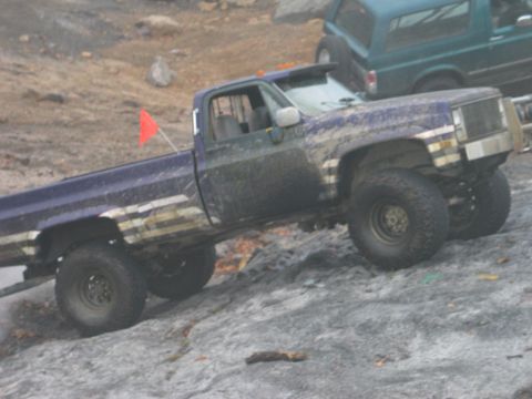 1995 Ford Bronco - A purple pickup truck navigates a rocky, off-road course, with another SUV visible in the background.
