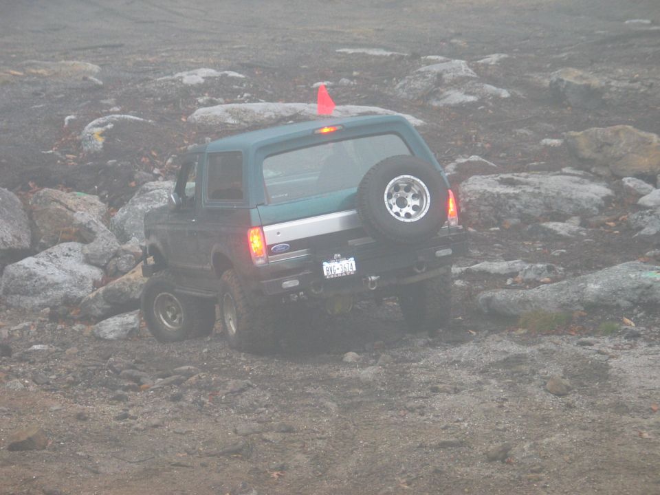 Green 1995 Ford Bronco with spare tire on rear, navigating rocky terrain