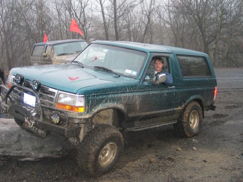 1995 Ford Bronco - A green 1995 Ford Bronco navigates an off-road obstacle with another vehicle visible in the background.