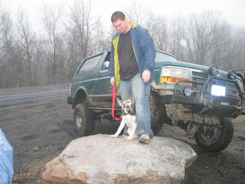 1995 Ford Bronco - Man and dog pose with a lifted green Ford Bronco on a rocky, muddy terrain.