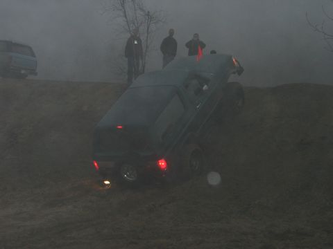 1995 Ford Bronco - An SUV navigates a steep, muddy incline on a foggy day, observed by several individuals.