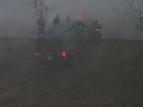 1995 Ford Bronco - A dark SUV navigates a steep dirt incline with several people observing.
