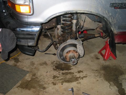 1995 Ford Bronco - Front suspension and wheel assembly of a 1995 Ford Bronco, supported by jack stands in a garage.