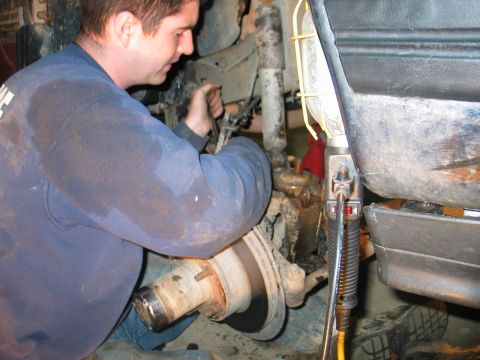1995 Ford Bronco - A mechanic is shown working on the suspension of a vehicle, illuminated by a work light.
