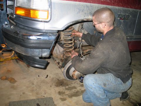 1995 Ford Bronco - A mechanic works on the front suspension of a 1995 Ford Bronco, focusing on the coil spring.