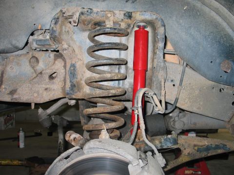 1995 Ford Bronco - The vehicle's suspension system, a coil spring and a red shock absorber, shows signs of wear and tear.