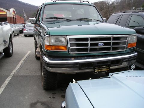 1996 Ford Bronco - A green Ford Bronco is parked in a lot, showing its front grille and headlights.