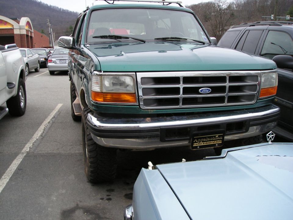 Green Ford Bronco parked in a lot. It has a roof rack and aftermarket wheels