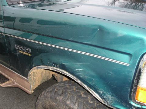 1996 Ford Bronco - Close-up of a green 1996 Ford Bronco's front fender, showing damage and the 'Bronco' badge.