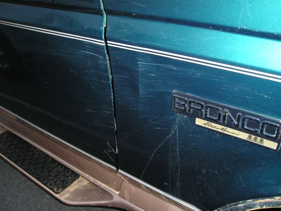 1996 Ford Bronco Eddie Bauer door panel with extensive scratches and a chrome trim strip