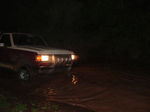 1990 Ford Bronco - A two-tone red and white 1990 Ford Bronco navigates through a flooded road in the dark.