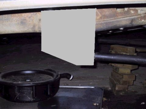 1979 Ford Bronco - The underside of a vehicle is shown with an oil drain pan and wooden blocks supporting a pipe.