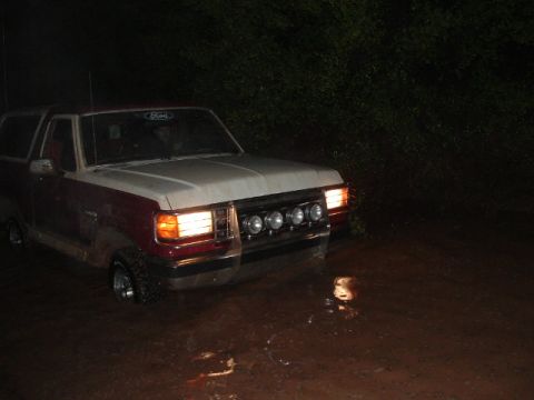 1990 Ford Bronco - This two-tone Ford Bronco is navigating a muddy terrain in the dark, with its headlights illuminating the path.