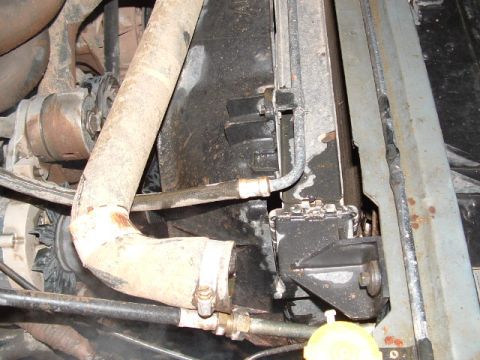 1990 Ford Bronco - Close-up down into the front corner of an engine bay showing a dusty upper radiator hose sweeping across the frame toward the radiator, wit…