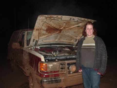 1990 Ford Bronco - A woman stands next to a muddy Ford Bronco with its hood open, taken at night.