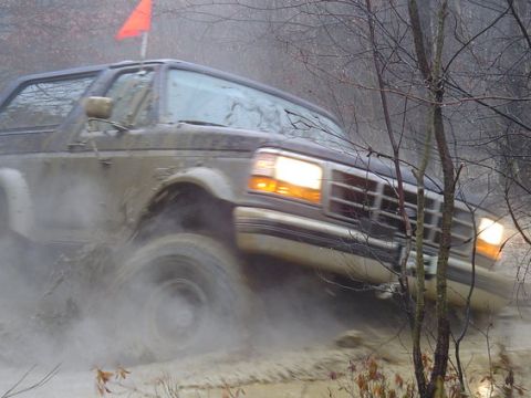 1995 Ford Bronco - A dark SUV navigates a muddy trail, kicking up water and spray.