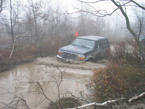 1995 Ford Bronco - A Ford Bronco navigates a challenging muddy trail, with a red flag visible on its roof.