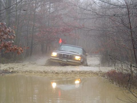 1995 Ford Bronco - A 1995 Ford Bronco navigates a muddy obstacle course in a wooded environment.