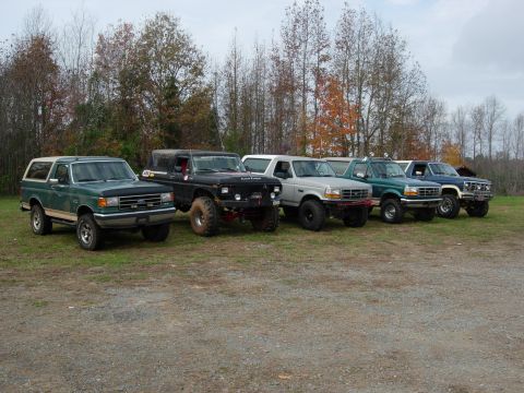 1995 Ford Bronco - A group of Ford Broncos, including a green 1995 model, are lined up outdoors on a gravel lot.