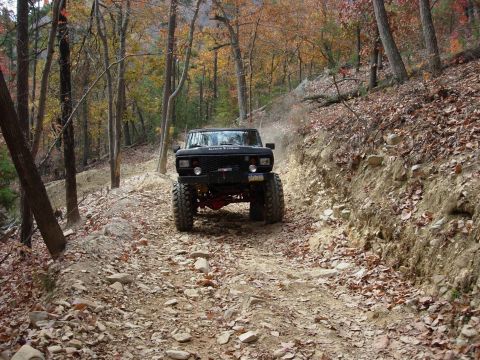 1995 Ford Bronco - A modified black SUV navigates a challenging off-road path surrounded by fall foliage.